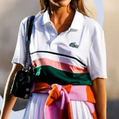 Frau trägt weißes Lacoste Poloshirt mit Streifen, schwarze Tasche und bunte Strickjacke um die Taille gebunden.